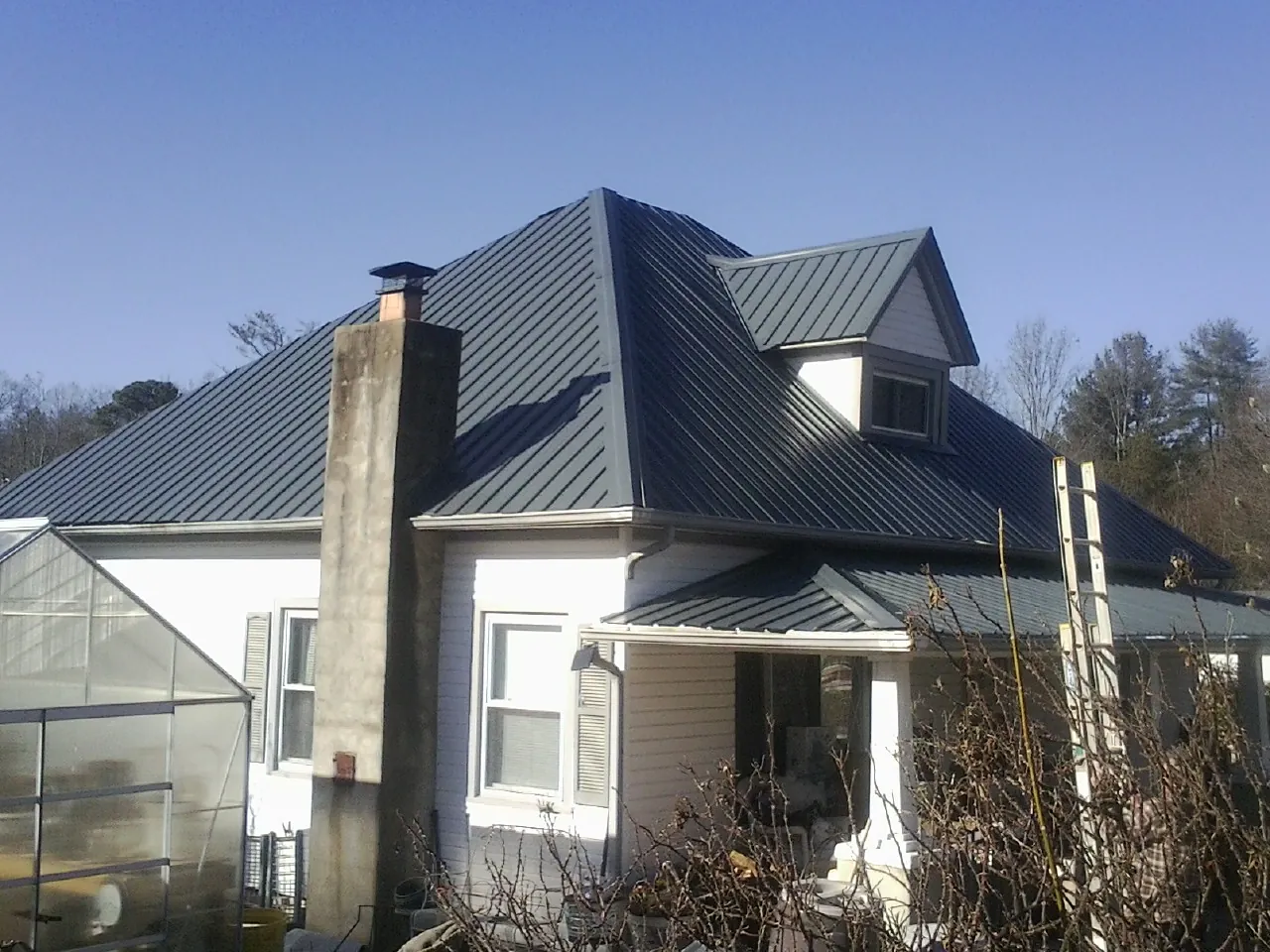 Dark blue standing seam metal roof on a white farmhouse with dormer — Slate & Tile Roof Repair by Roofing Brothers in Kalona