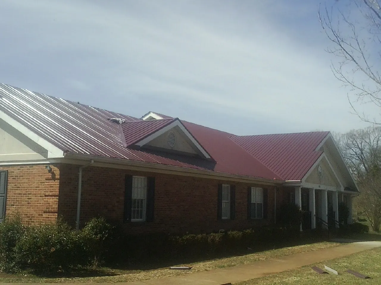 Red metal roof with gabled entries on a long brick building, from a Hail Damage Roof Repair job in Kalona