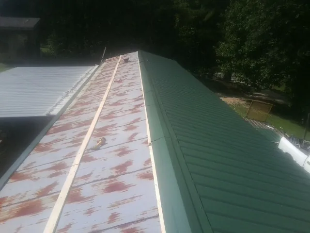 Old rusted panels beside newly installed green metal roofing — Wind Damage Roof Repair by Roofing Brothers in Kalona