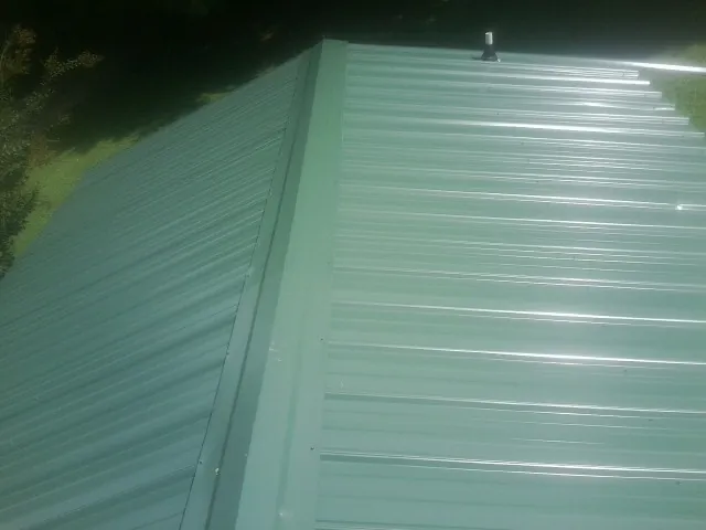 New green metal panels meeting at the ridge of a roof — Flat Roof Repair work by our crew in Kalona