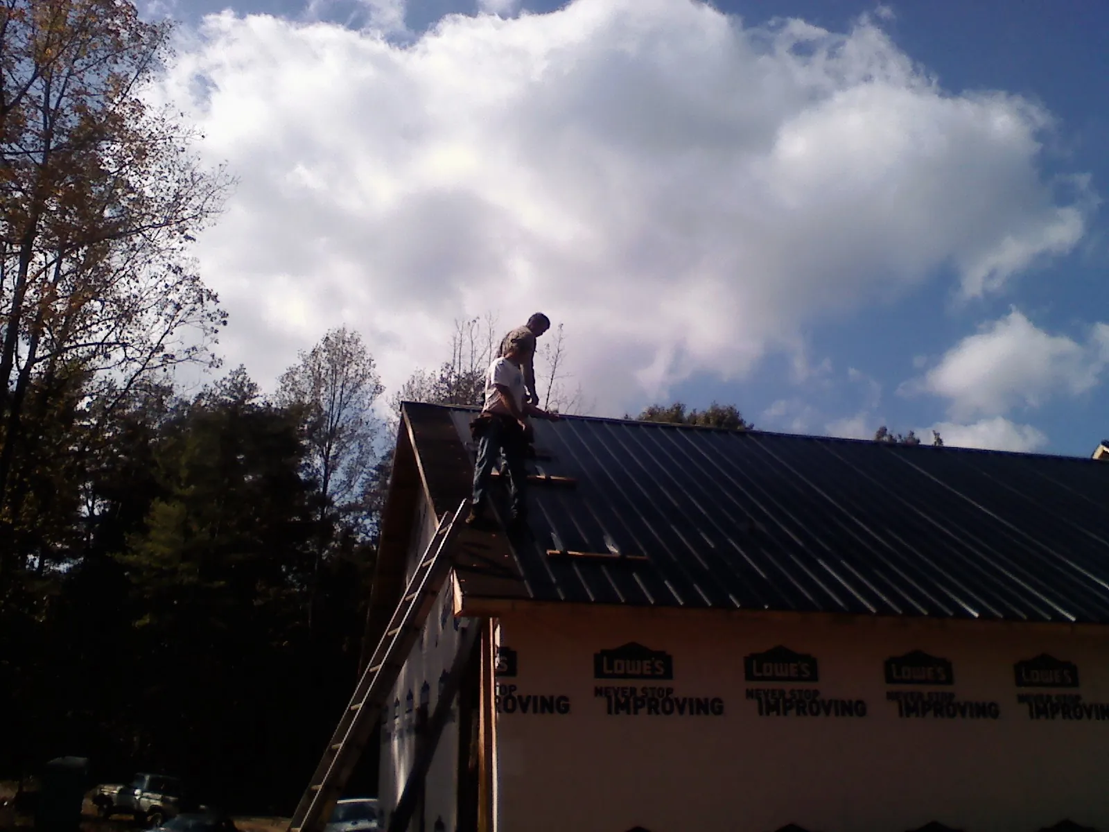 Roofer fastening dark metal panels high against a cloudy sky, from a Roof Inspection job in Kalona