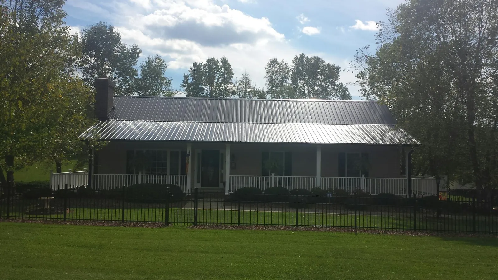 Gray metal roof on a brick ranch with a full width front porch — Gutter Guard Installation work by our crew in Kalona