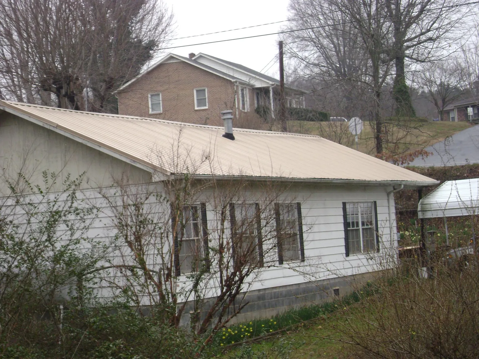 Tan metal roof on a white sided house set into a hillside — Commercial Roofing by Roofing Brothers in Kalona