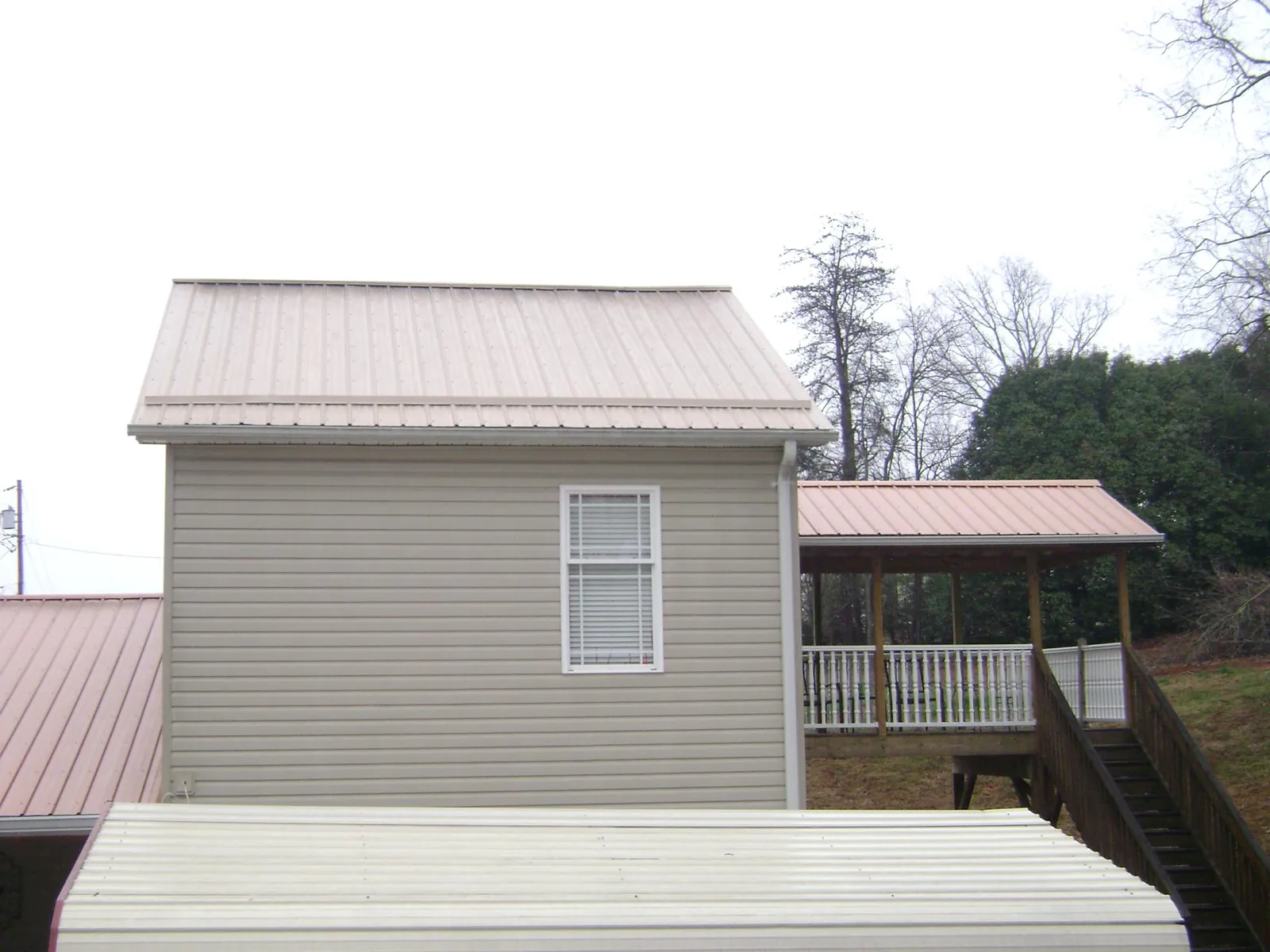 Tan metal roofs on a two story addition and attached porch, from a Roof Replacement job in Kalona