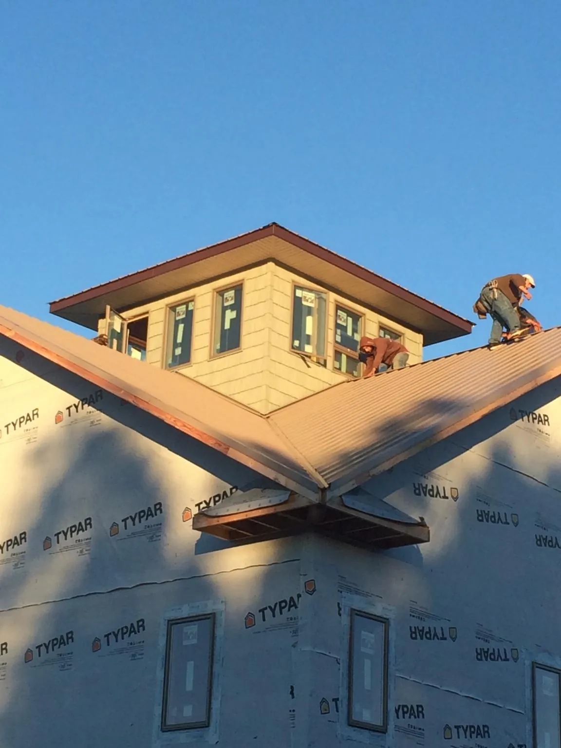 Roofers working around a rooftop cupola on a new metal roof at sunset — Roof Waterproofing in Kalona by Roofing Brothers